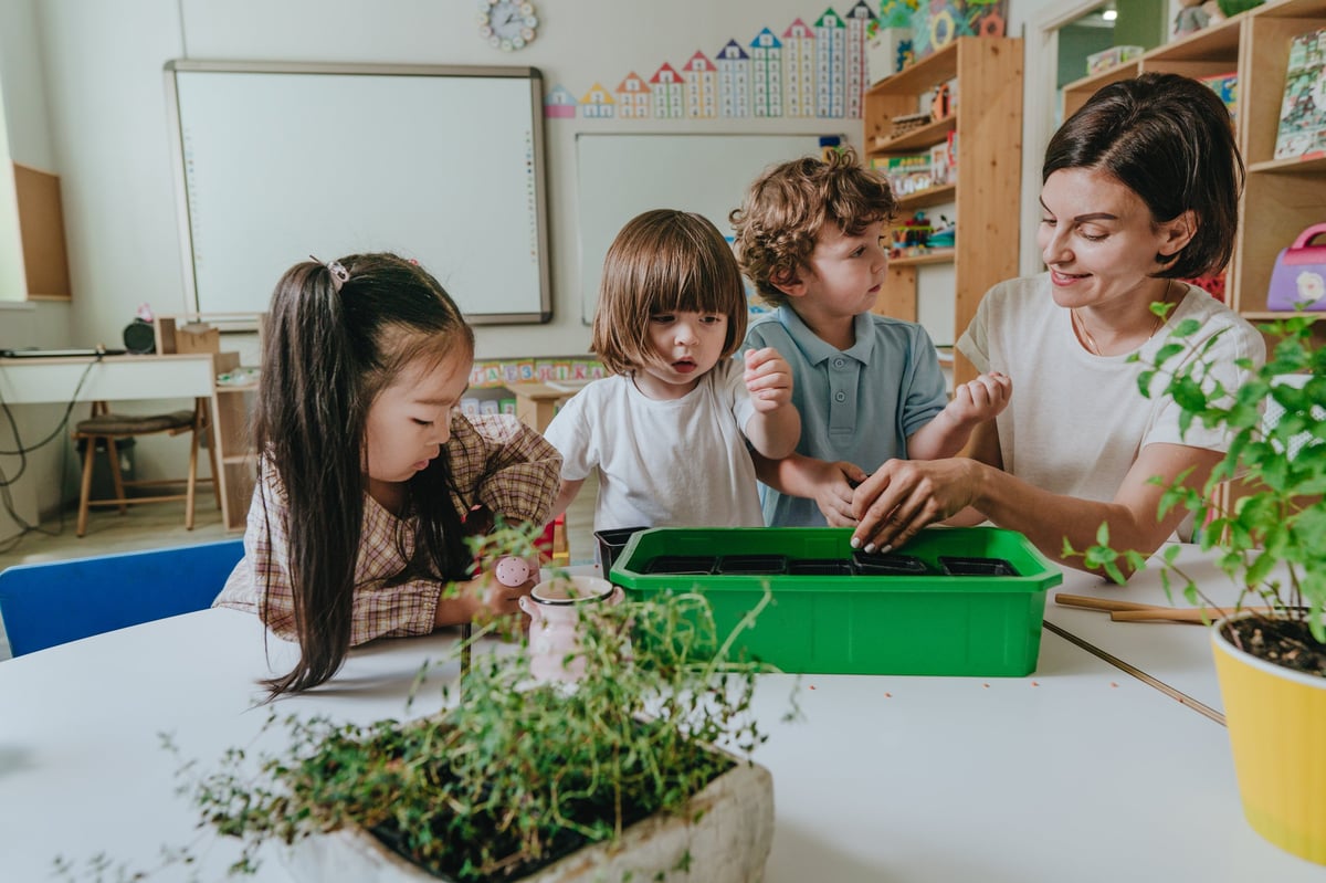 Maestra joven con niños plantando una planta en maceta