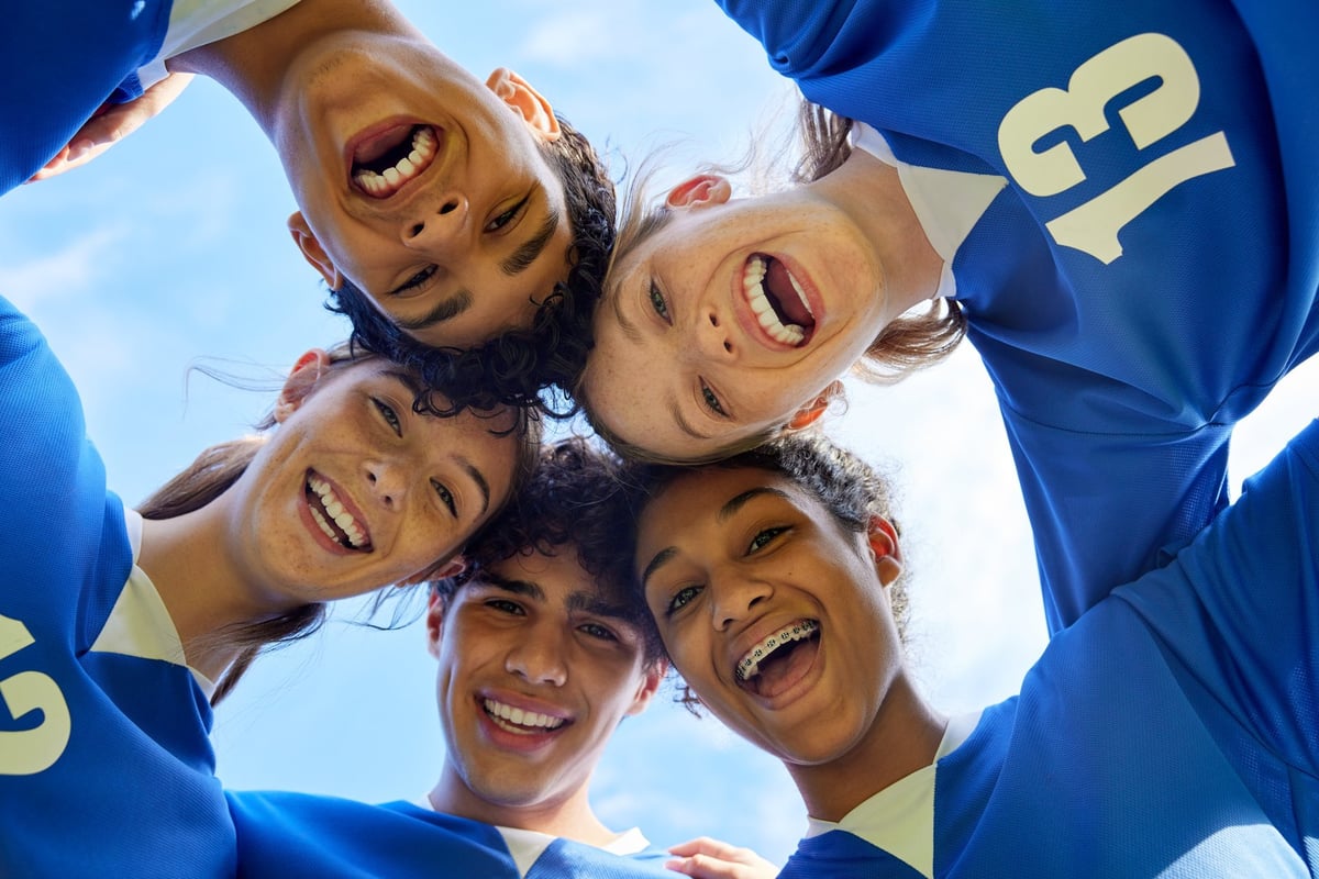 Portrait of young sports team in a close huddle smiling. Group of guys and girls forming a circle with happy faces.