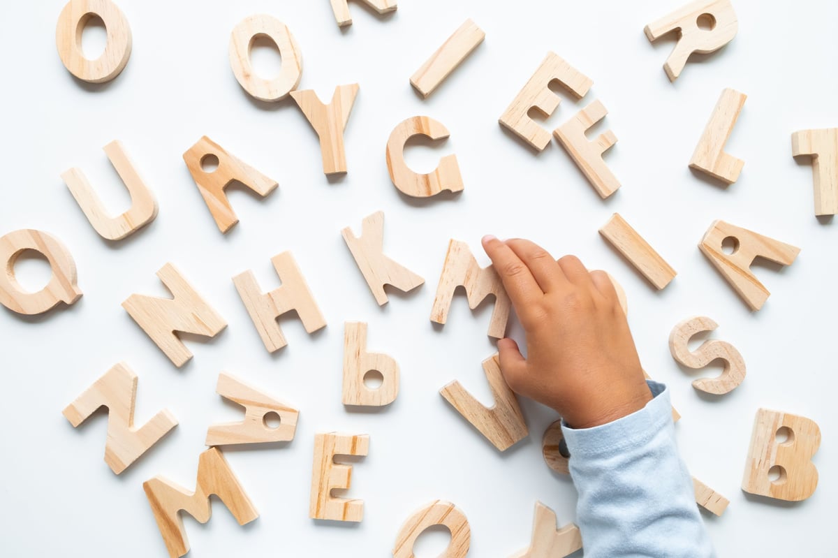 Mano de niño ordenando letras del alfabeto de madera sobre superficie blanca