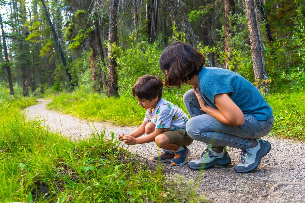 Madre e hijo agachados examinando una pequeña flor púrpura en el bosque