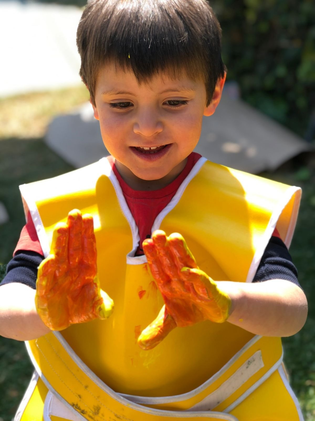 Smiling young boy wearing a yellow safety vest with paint-covered hands raised in front of him