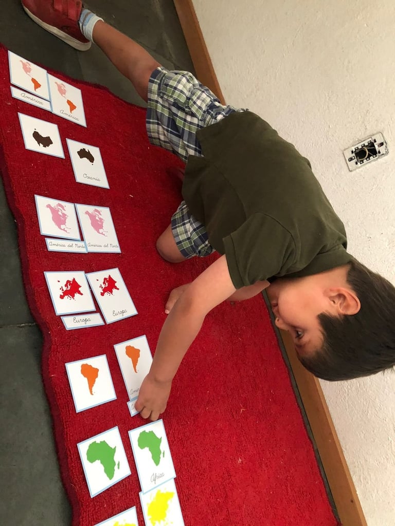 Person pointing at colorful shape cards arranged on a red mat for a matching activity