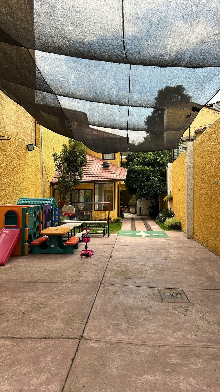 Outdoor school playground with colorful play equipment, shaded courtyard with yellow walls and dark shade cloth overhead
